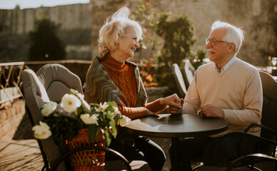 Senior couple holding hands in the outdoor cafe on a sunny autumn day - Powered by Adobe