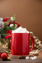 Hot chocolate or warm winter drink in red mug with marshmallows. Christmas decoration on wooden background, copy space