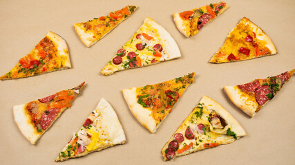 Grop of triangular slices of different types of pizza on a beige kraft paper background.