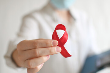 Concept World AIDS and hiv day. A female doctor in a white coat holds red ribbon on white...