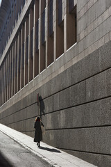 A woman dressed in a winter coat walking facing a  granite facade.