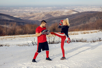 Sportswoman sparring with boxing gloves in nature at snowy winter day with her instructor. She is...