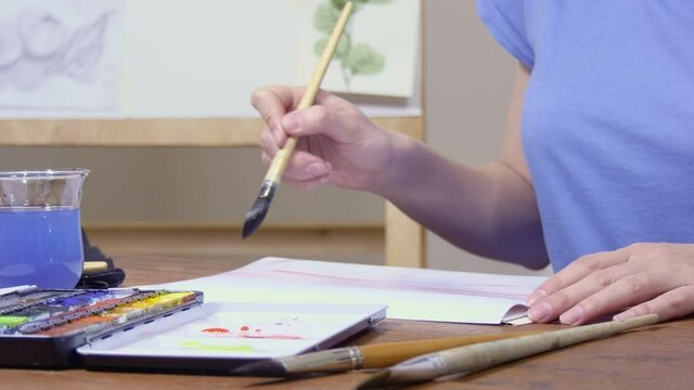 The artist applies watercolor paint to the brush and draws.