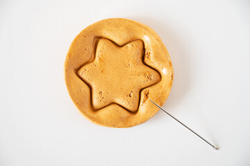 Brown sugar caramel candy cookies with a metal needle in the shape of a star on a white background.