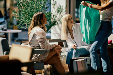 Three young women looking at beautiful clothing they bought at a shopping mall on Black Friday. Coffee shop interior.