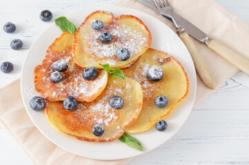 pancakes with blueberries, powdered sugar and mint on a plate, beige napkin, fork, knife  on a white background