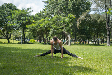 Sporty active young man in sportswear doing sport exercises in the park. Fit caucasian man stretching on the grass outdoors. Healthy lifestyle concept