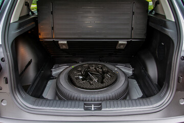 Spare wheel in the trunk of a modern car. Jack lifting and a spare tire in rear of car. - obrazy, fototapety, plakaty