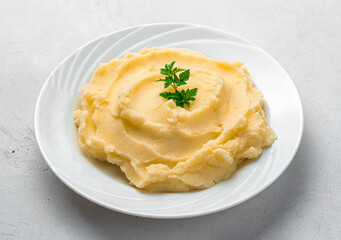 Mashed potatoes with basil in a white plate close-up on a gray background.
