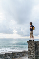Panoramic view of young traveler man sightseeing in a cliff. Vertical view of backpacker traveling outdoors with the blue ocean on the background.