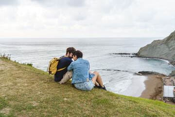 Fototapeta na wymiar Couple in love hiking and sit in a cliff in Guipuzcoa. Horizontal view of backpackers sightseeing in holidays in Zumaia beach. Spanish people and travel concept.
