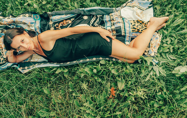 Beautiful woman lying on the green grass with black hair. The woman is at rest and looking at the camera.Short black dress