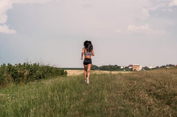 Naklejka na ściany i meble Beautiful woman running across the field. Short black shorts, top. Rear view