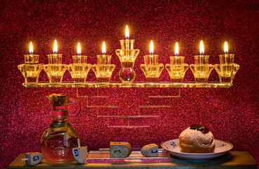 Image depicts Jewish holiday Hanukkah with menorah and burning candles, jar with olive oil, sweet donut. Hebrew letters on  dreidels mean - Great Miracle Happened Here. Blurred festive backgrounds