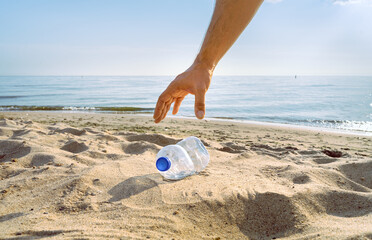 A hand reaches to pick up a discarded water bottle on a beach