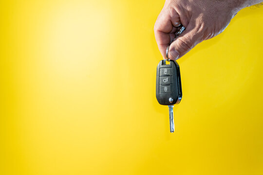 Male hand holds the black keys of a car, isolated on yellow background.