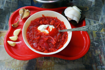  On a red tray is a plate of borscht with a spoonful of sour cream, and next to it lies lard on...
