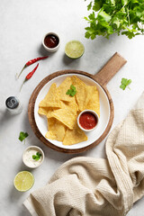 Corn chips nachos with salsa and cheese sauce, fresh herb, lime and chili pepper on white background. Concept Mexican food. Top view and copy space