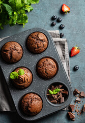 chocolate muffins with blueberry and strawberry slices in a baking dish on a dark  background. Top view