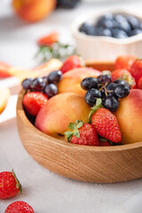 Fresh organic summer berries and fruits of strawberries, blueberries, peaches and grapes in a  wooden plate on a white background. Macro and close up