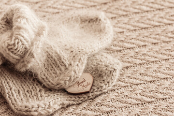 White Woolen knitted baby socks on beige textured knitted background.  Sign Handmade. Warm handmade knitwear. Top view