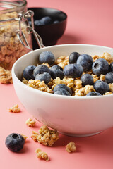Granola with blueberry in white bowl on pink background.