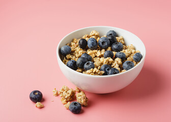 Granola with blueberry in bowl on pink background.