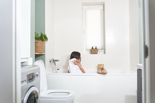 Side shot of a woman sitting in the bathroom. The girl wipes her hair with a white towel. High quality photo