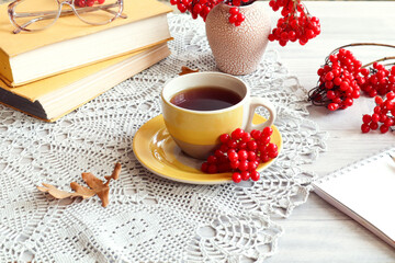 Cozy autumn days: a yellow mug with tea, viburnum branches with red berries, books, a notebook on a gray napkin, side view