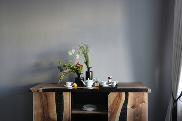 Beautiful contemporary art composition with artifitial flowers, vases, tea set and objects on a wooden chest of drawers