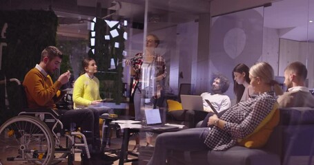 Disabled businessman in a wheelchair at work in modern open space coworking office on team meeting using virtual reality goggles and drone simulation. Effective teamwork in a startup business. - Powered by Adobe