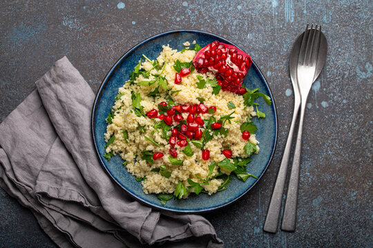 Bright colourful couscous or bulgur salad with pomegranate seeds Tabbouleh in rustic blue ceramic bowl top view on concrete background, traditional middle eastern or arab dish with space for text

