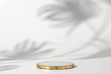 Marble podium with gold on the white background with shadow of tropical plant. Podium for product,...