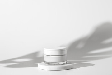 White unbranded cosmetic cream jar standing on white podium. Skin care product presentation on the...