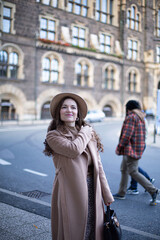 Naklejka premium Pretty woman with curly hair in old town dressed in autumn coat and a hat