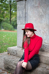 White woman with long dark hair in bright red sitting near the monument in park