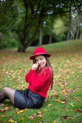 White woman with long dark hair in bright red in fall park sitting on the grass