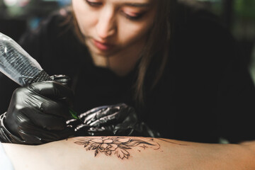 Woman tattoo artist doing tattoo in studio, making tattoo on body. closeup