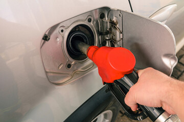 Pumping petrol at gas station into vehicle. Hand holding a red pistol to refuel car with gasoline.