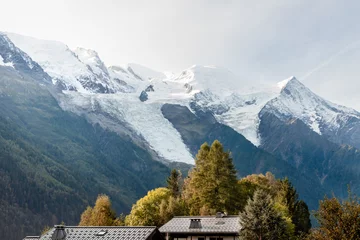 Poster de jardin  Rooftops and pine trees with snow-capped mountains at sunrise  © PGS