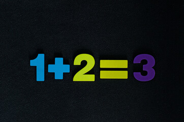 Simple mathematical equation made from colorful wooden numbers on black background	