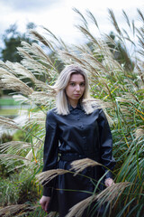 European blond young woman in black autumn dress with reeds behind