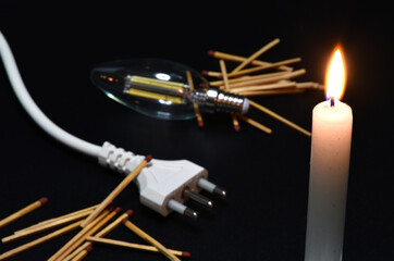 close-up on a lit candle along with a power cord, light bulb and matches on a black background