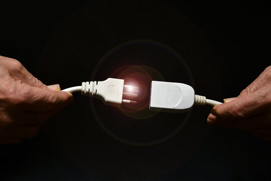 a man holds two disconnected electric cables in his hand on black background. electricity supply problem concept. blackout
