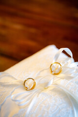 Side view two tiny golden wedding rings on white cushion with wooden floor background