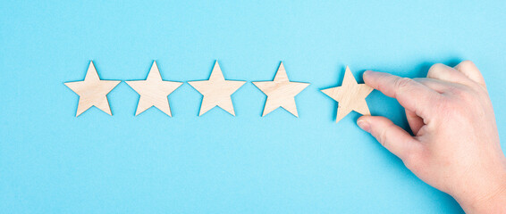 Five stars on a blue colored background, hand put the last star in the row, rating, giving feedback