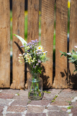 Low angle view spring flowers in glass jar standing on ground by fence in sunny daylight