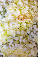 Tow view two golden wedding rings on white flower bouquet background