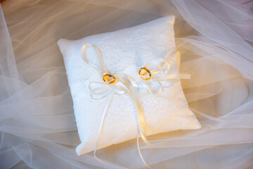 Top down view square white pillow with two golden wedding rings with ribbons on display