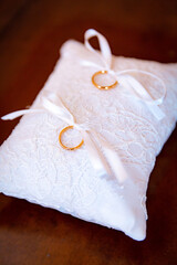 Vertical image of two golden wedding ring lay on white decorative cushion for bride and groom on weddings